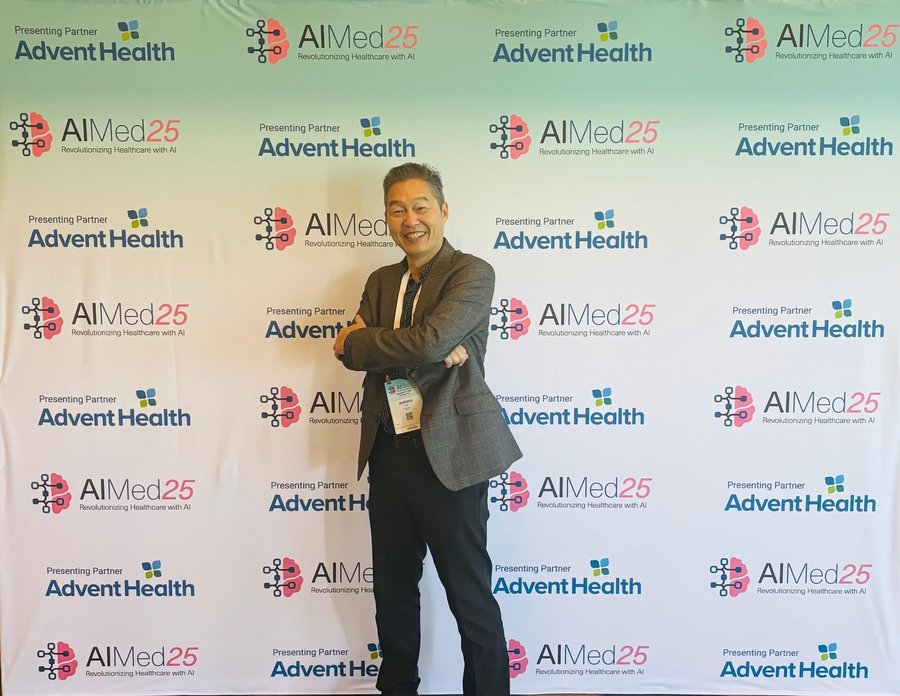 Anthony Lee smiling in front of an AIMed25 and AdventHealth step-and-repeat backdrop.