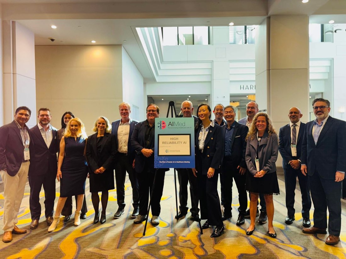 Group photo of TTIC leadership and speakers at AIMed 2025 holding a High Reliability AI track sign.